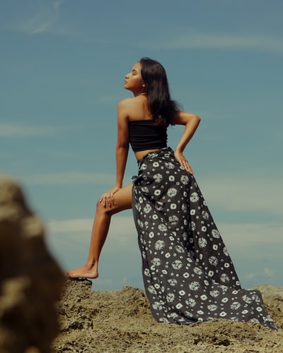 woman in black and white floral dress standing on brown rock during daytime